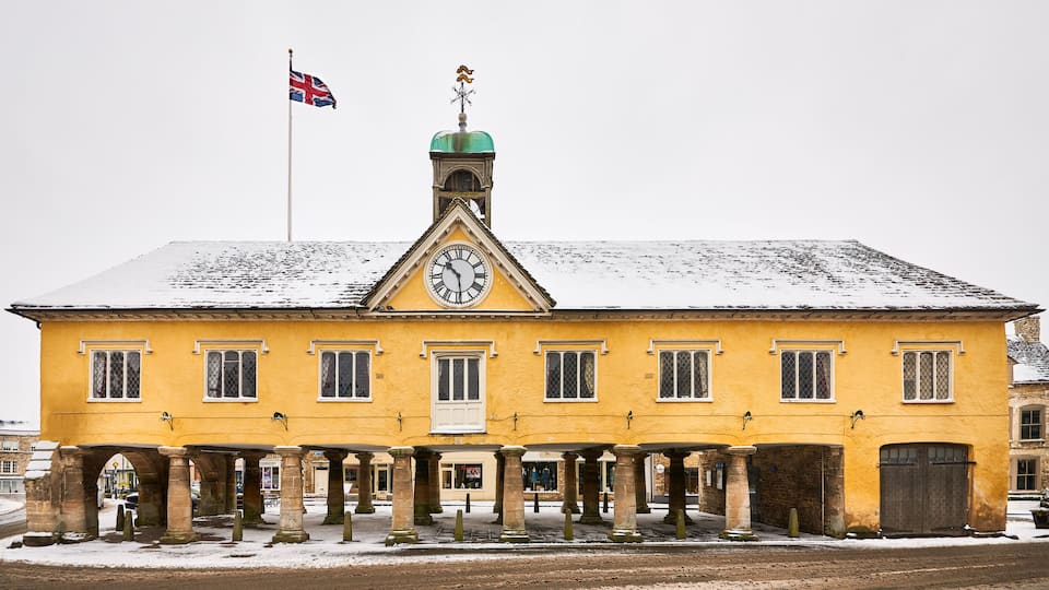 A yellow building with a clock tower, a flag, and snow on the roof.