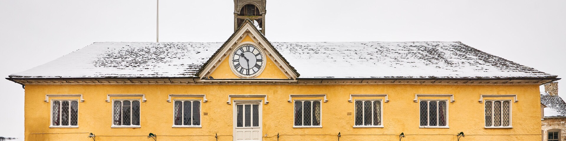 Un edificio amarillo con una torre de reloj, una bandera y nieve en el tejado.