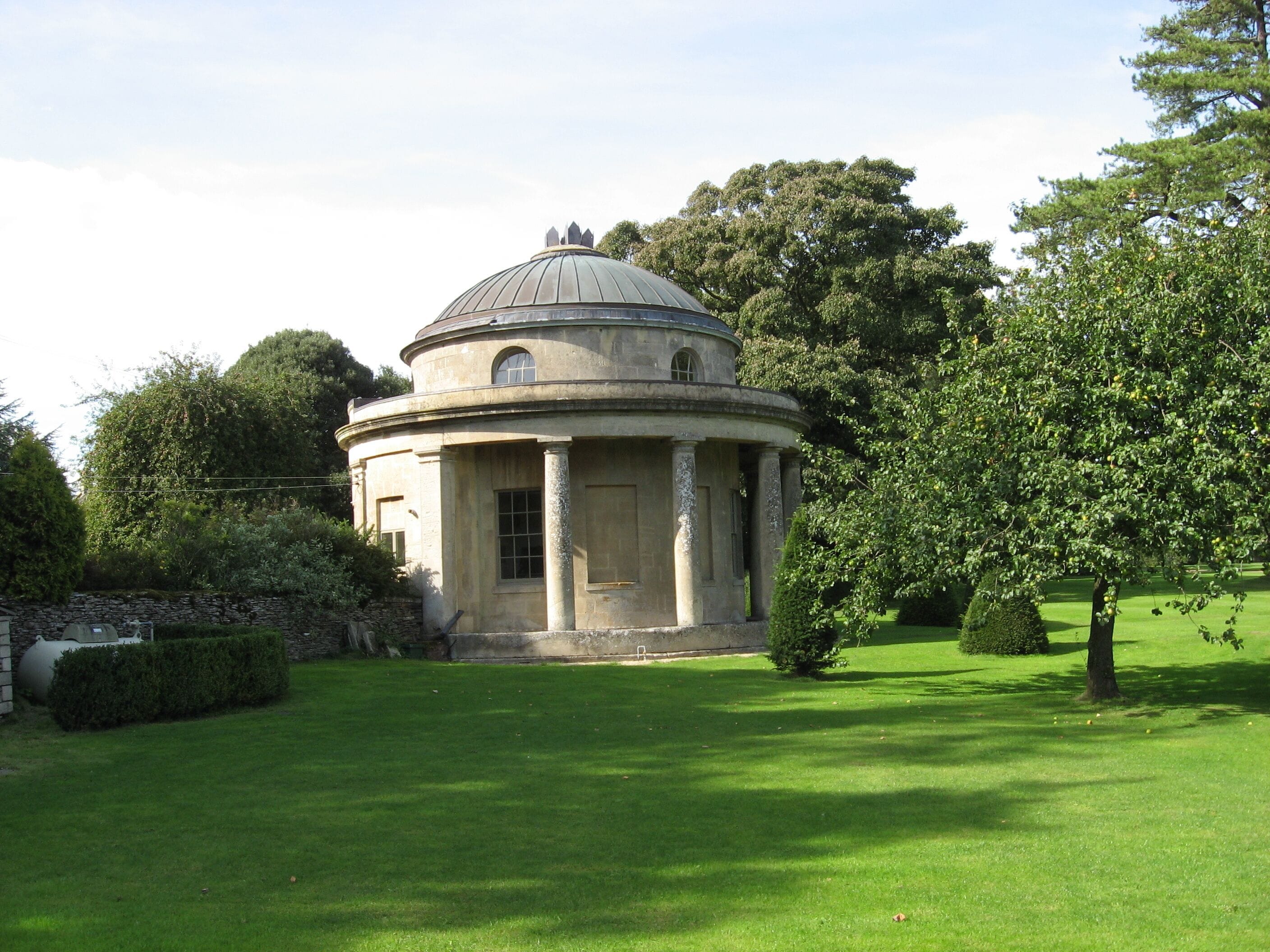 A classical building with a dome, surrounded by well-maintained grass and trees.