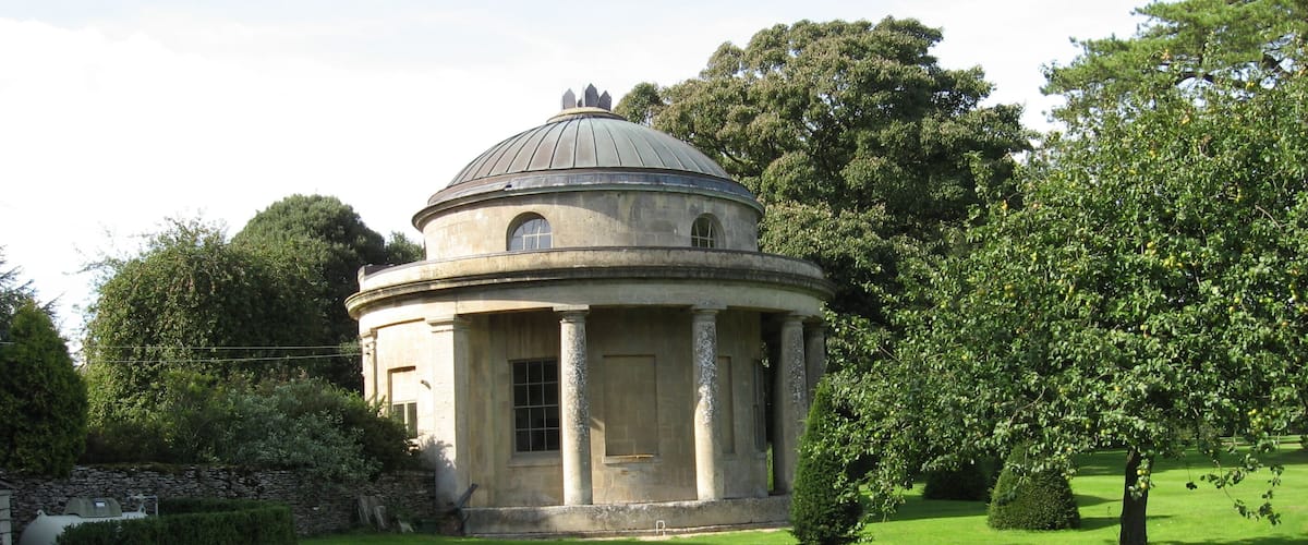 A classical building with a dome, surrounded by well-maintained grass and trees.