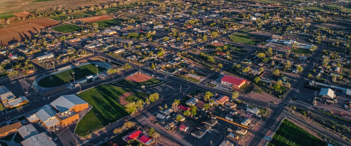 An aerial view of a town with a grid of streets, green fields, and buildings.