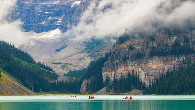 Un lago rodeado de montañas, con kayakistas en el agua y una cadena montañosa boscosa al fondo.