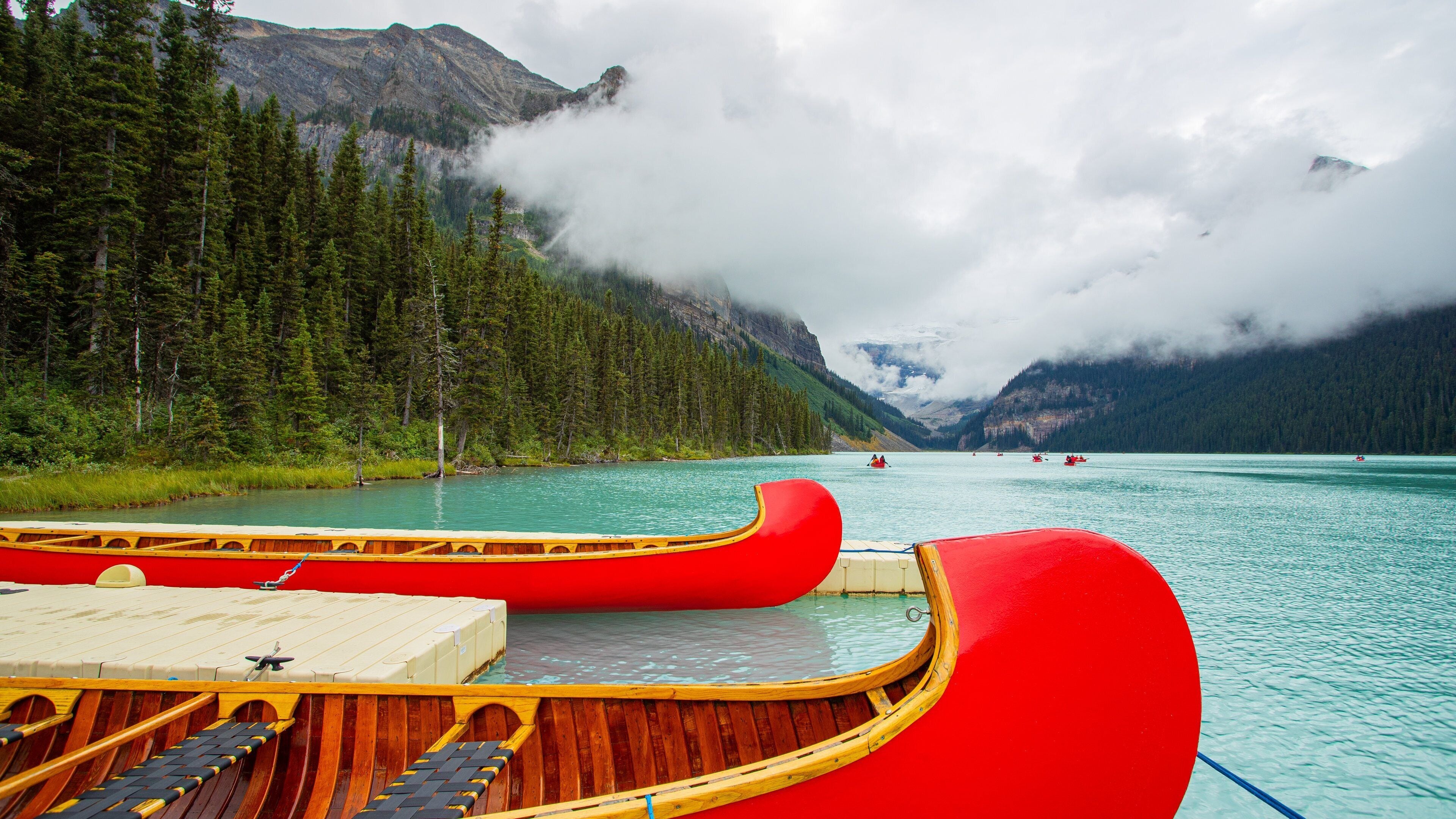 A calm lake with red boats, surrounded by dense forests and mountains.
