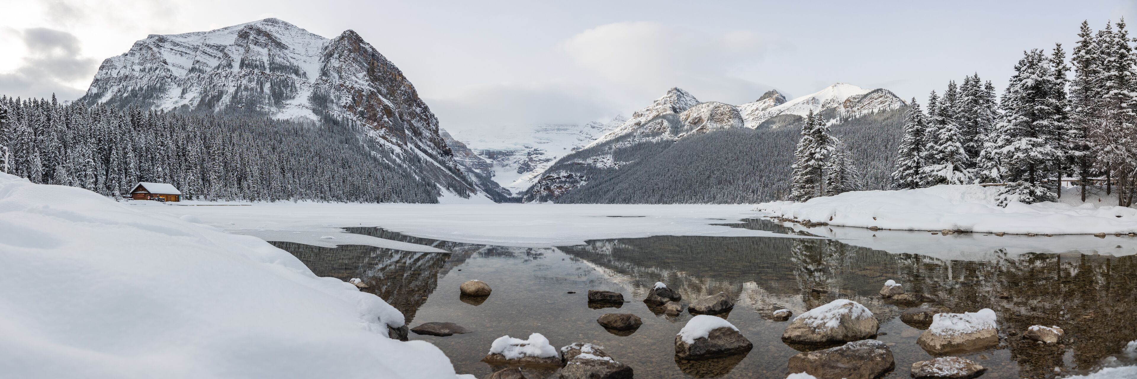 Incredible Lake Louise during winter time with scenic  landscape in panorama, panoramic view with snow covering the frozen lake area. 