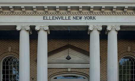 A building facade with the inscription "ELLENVILLE NEW YORK" above a series of classical columns and a triangular pediment.