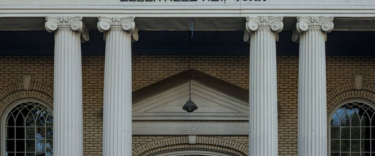 A building facade with the inscription "ELLENVILLE NEW YORK" above a series of classical columns and a triangular pediment.