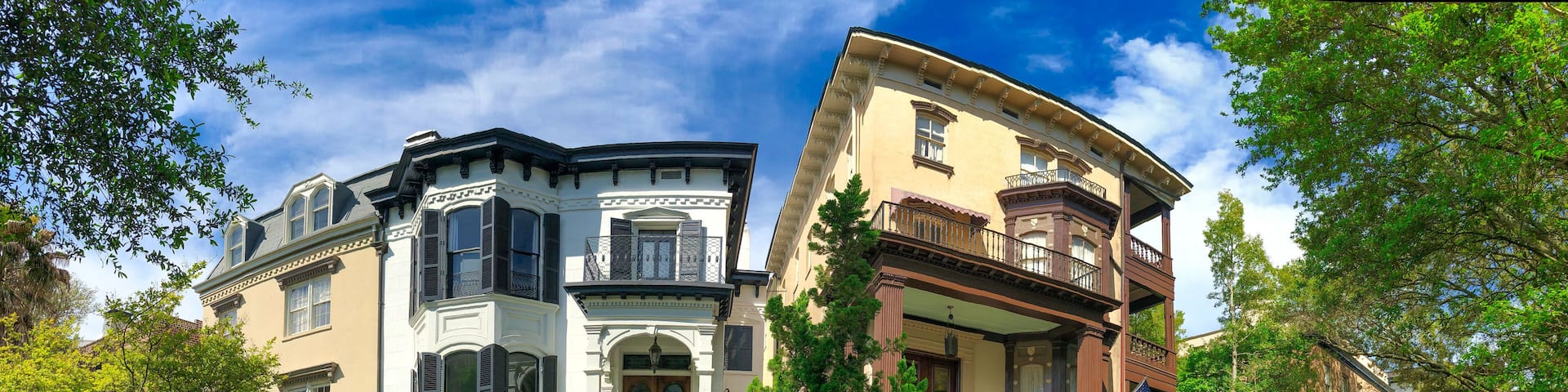 A row of historic houses with ornate facades, a clear blue sky, and lush greenery.