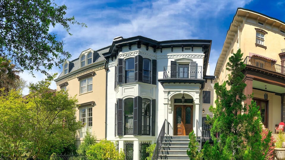 A row of historic houses with ornate facades, a clear blue sky, and lush greenery.