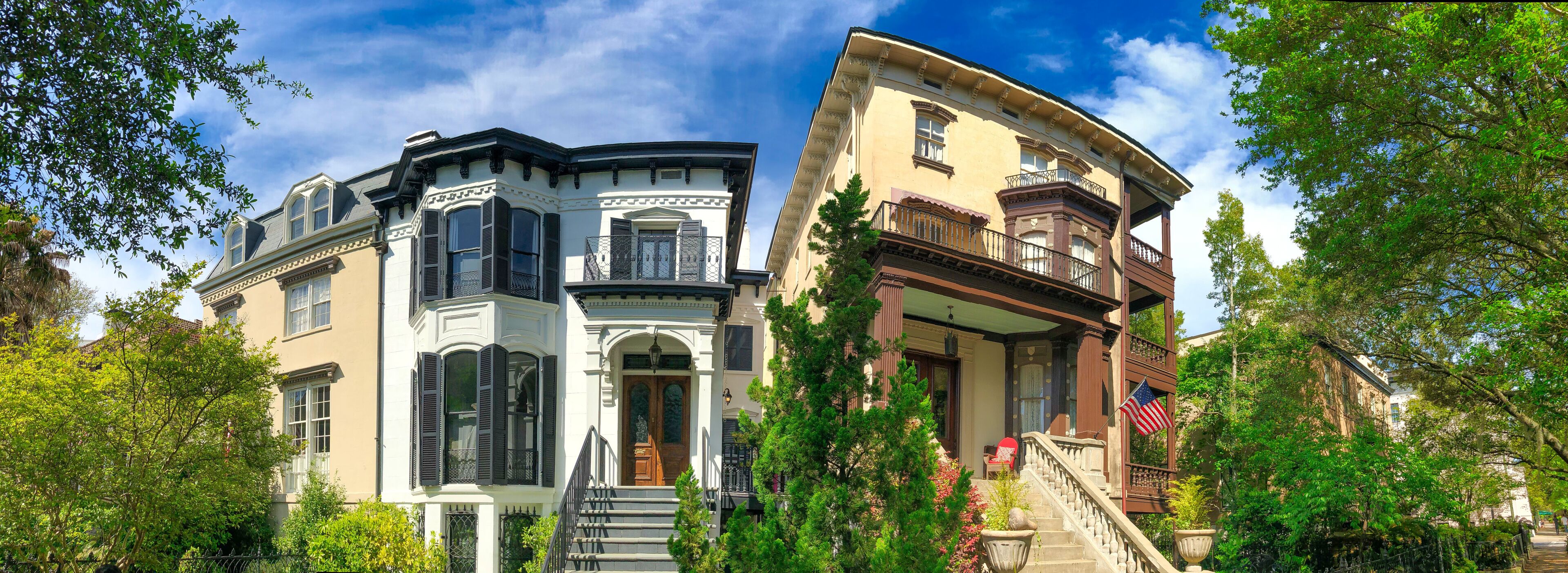 A row of historic houses with ornate facades, a clear blue sky, and lush greenery.
