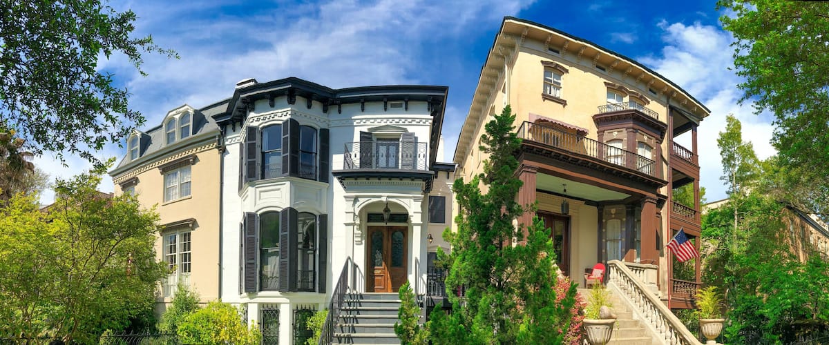 A row of historic houses with ornate facades, a clear blue sky, and lush greenery.