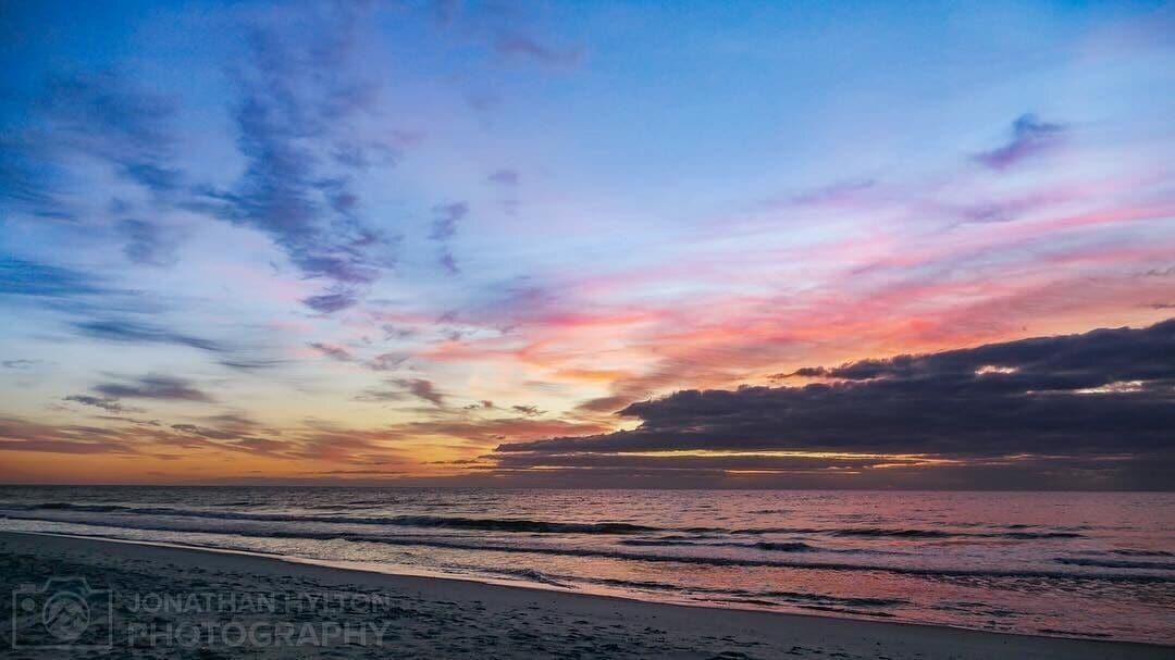 A beach at sunset with a colorful sky and ocean waves.
