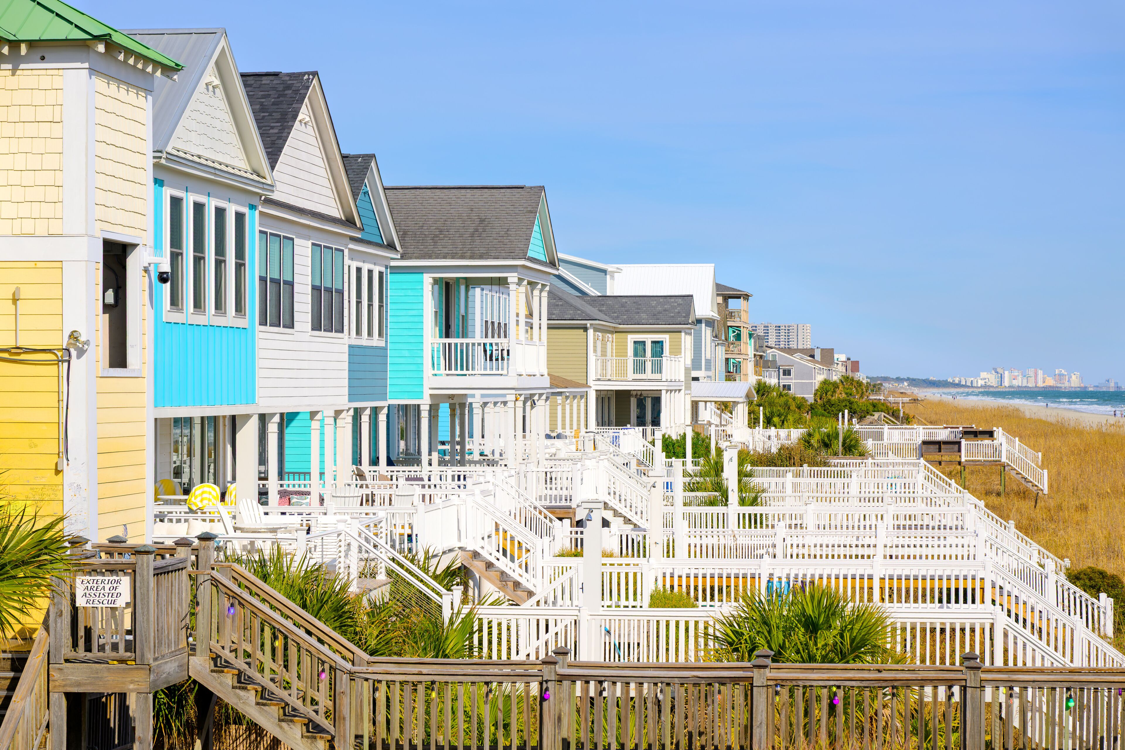 Colorful waterfront homes along the grassy dunes of the Atlantic Ocean with the Myrtle Beach skyline in the distance, in Surfside Beach, South Carolina.