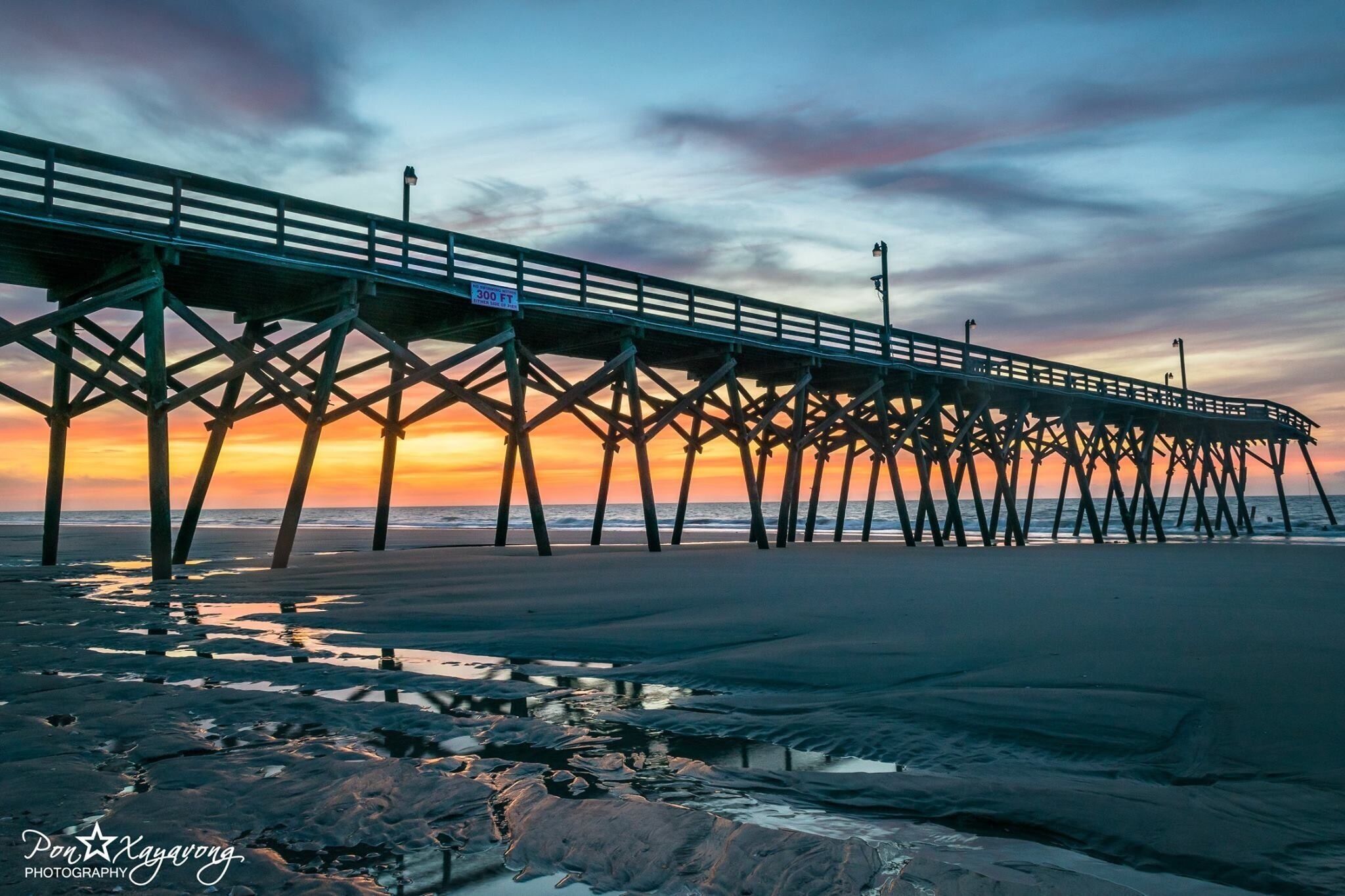 A pier extending over a beach at sunset.