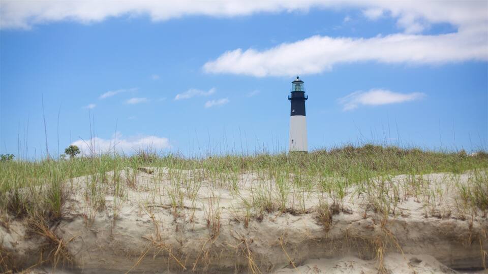 A lighthouse on a sandy dune with grass in the foreground and a clear blue sky.
