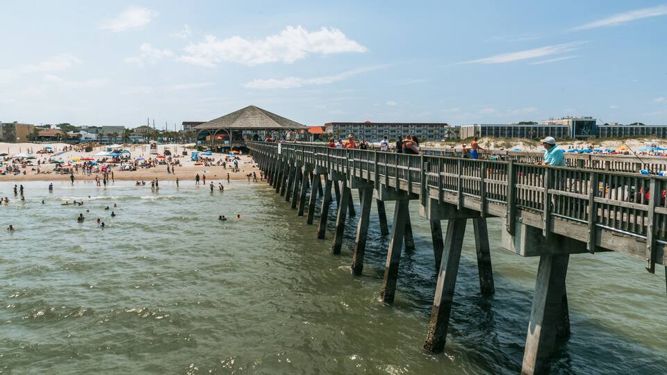 A pier extending into a beach with people swimming and sunbathing.