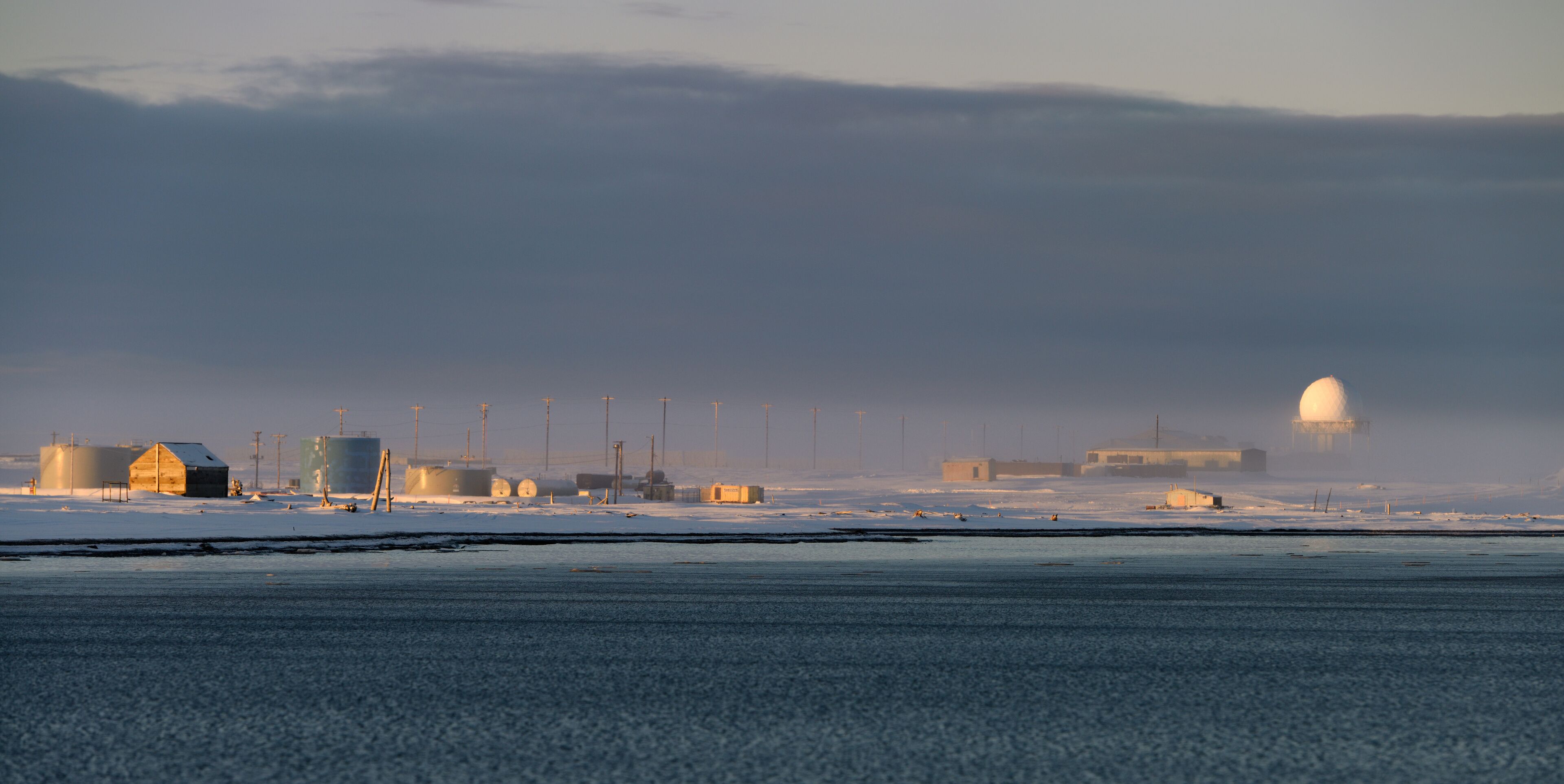 A snowy landscape with industrial buildings and storage tanks.