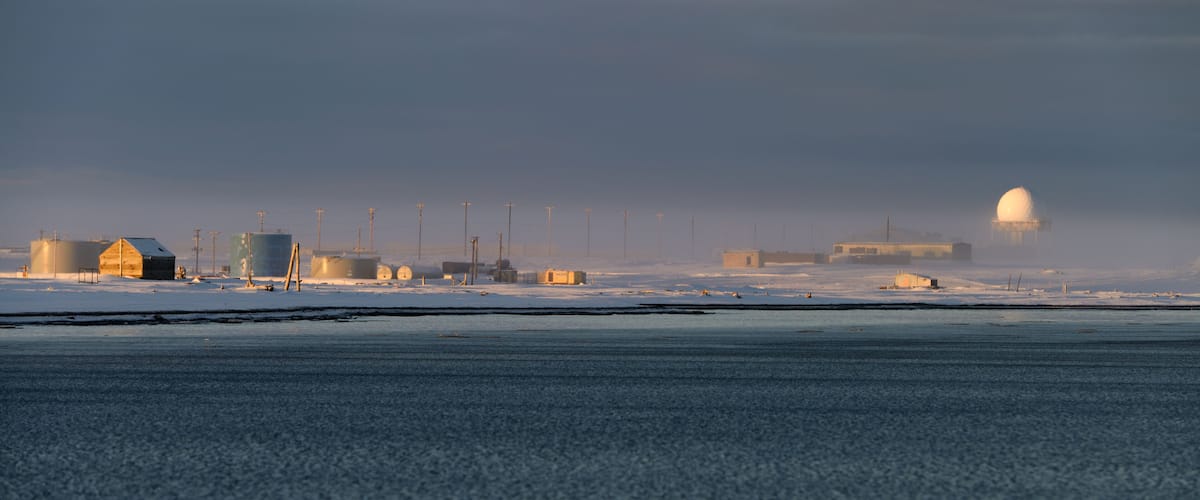 A snowy landscape with industrial buildings and storage tanks.