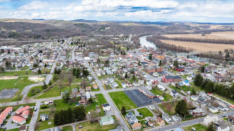 An aerial view of a town with a river, green spaces, and a mix of residential and commercial buildings.
