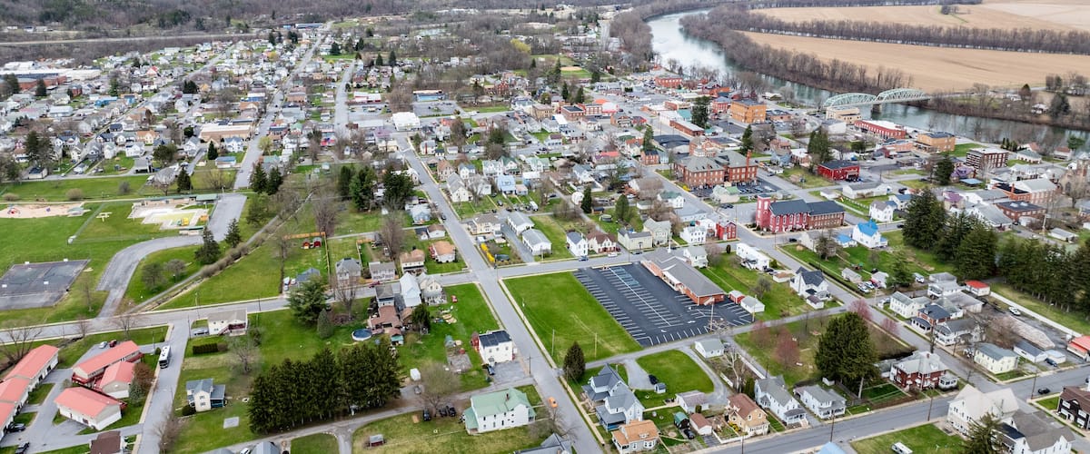 An aerial view of a town with a river, green spaces, and a mix of residential and commercial buildings.