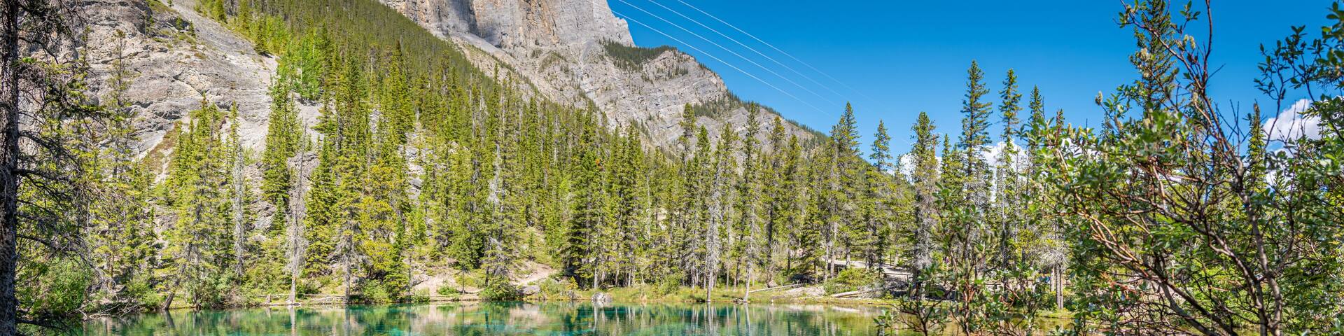 A mountain lake with clear turquoise water, surrounded by dense green forest and rocky cliffs.
