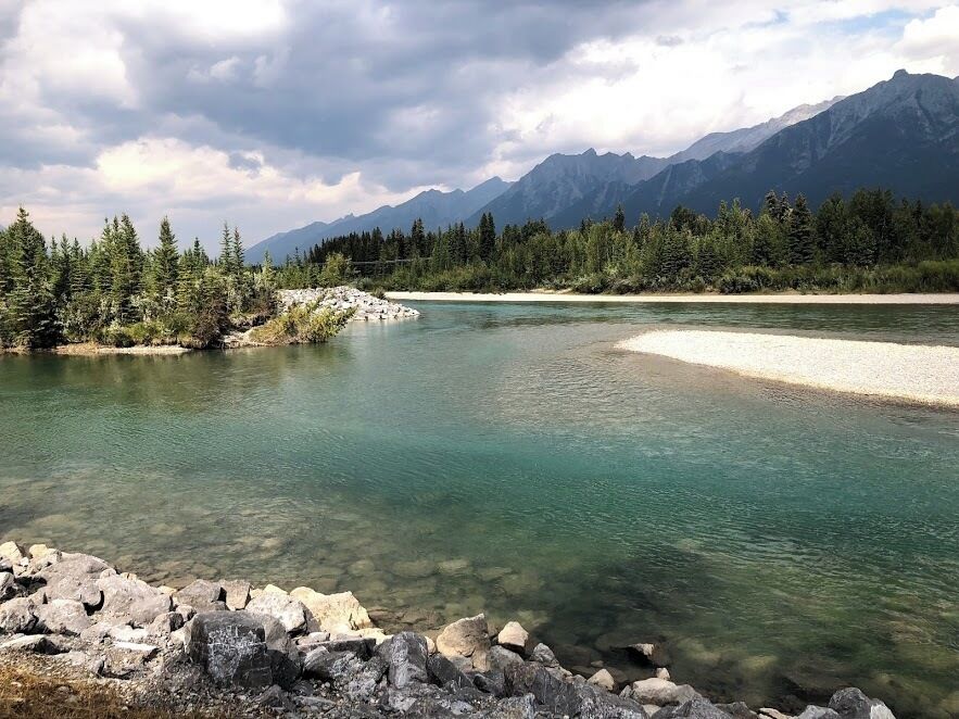 A clear river with rocky shores, surrounded by dense forest and mountains in the background.
