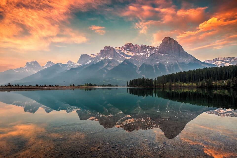A mountain range reflected in a calm lake with a clear sky.