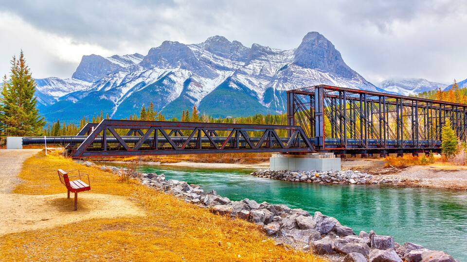 A metal bridge over a river with mountains in the background.