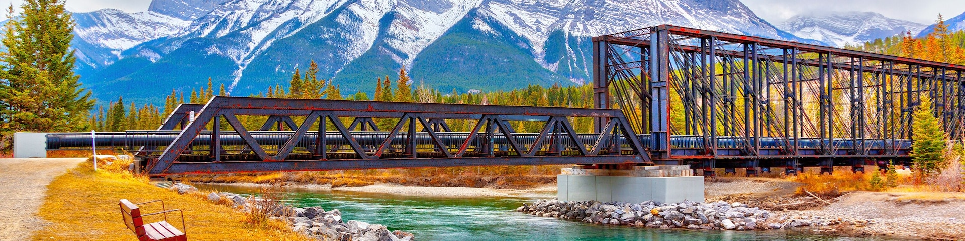 A metal bridge over a river with mountains in the background.