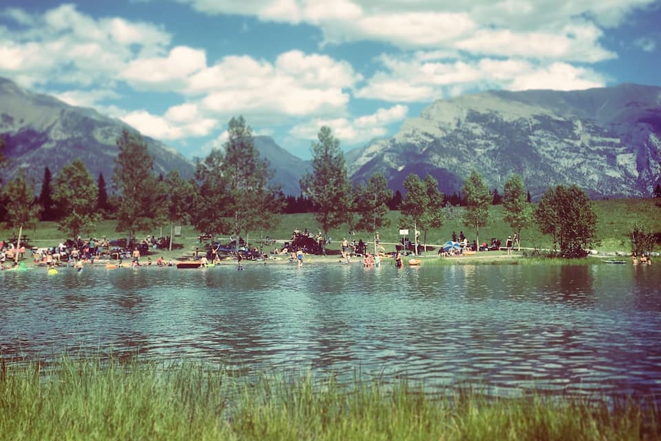 A lake with people swimming and sunbathing, surrounded by mountains and trees.