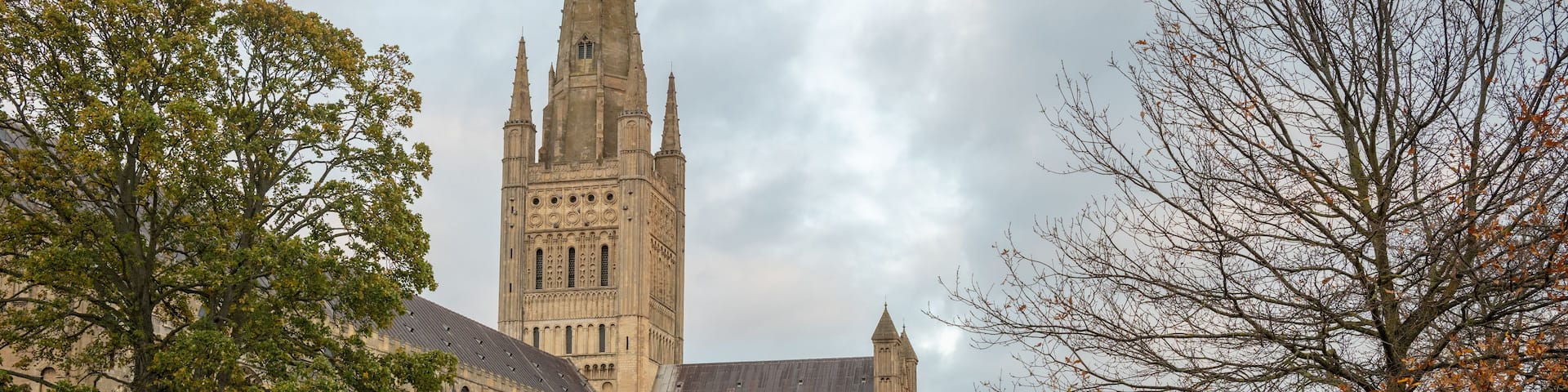 A historic cathedral with a tall spire, surrounded by trees and a covered walkway.