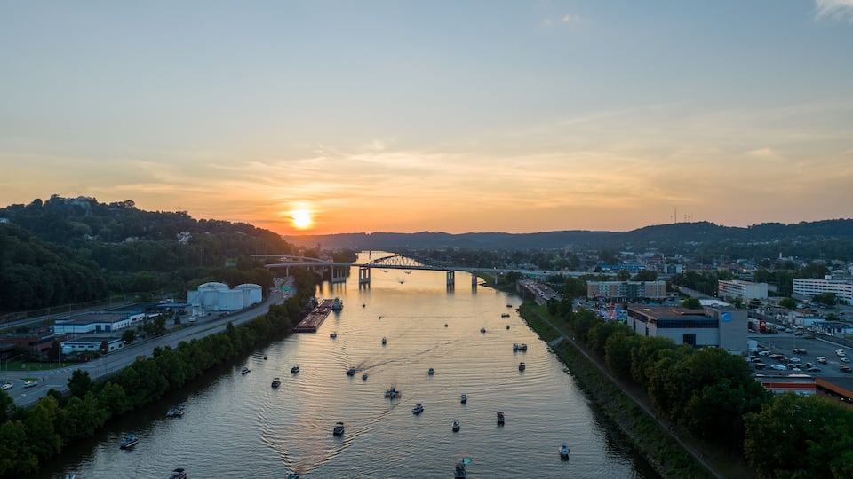 A river with boats, a bridge, and a cityscape at sunset.