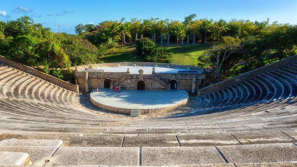 An outdoor amphitheater with stone steps and a central stage surrounded by trees.
