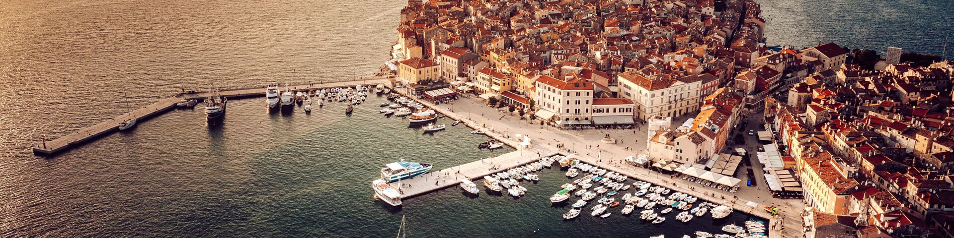 An aerial view of a coastal town with a dense cluster of buildings, a prominent tower, and a marina filled with boats.