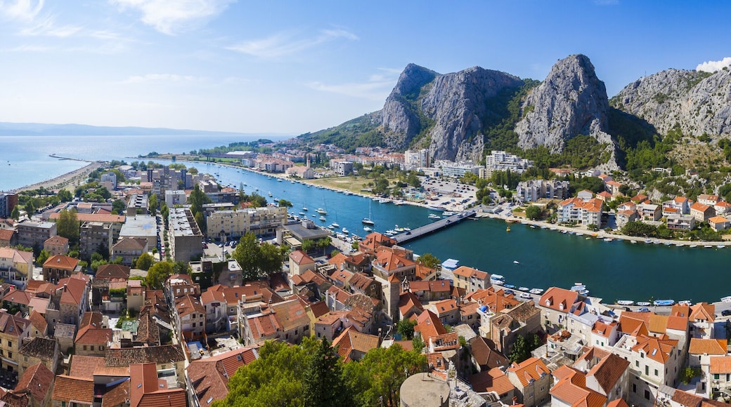 View of terracotta rooftops cascade toward the turquoise river, embraced by towering grey cliffs under a bright blue sky in Omis, Split-Dalmatia County, Croatia.