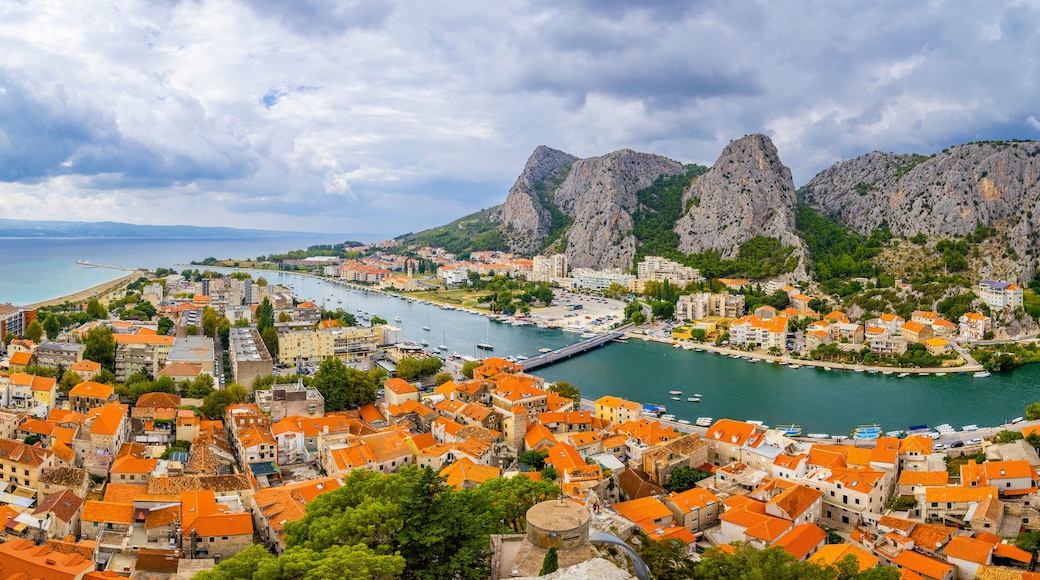 A coastal town with orange-roofed buildings, a marina, and rocky cliffs.