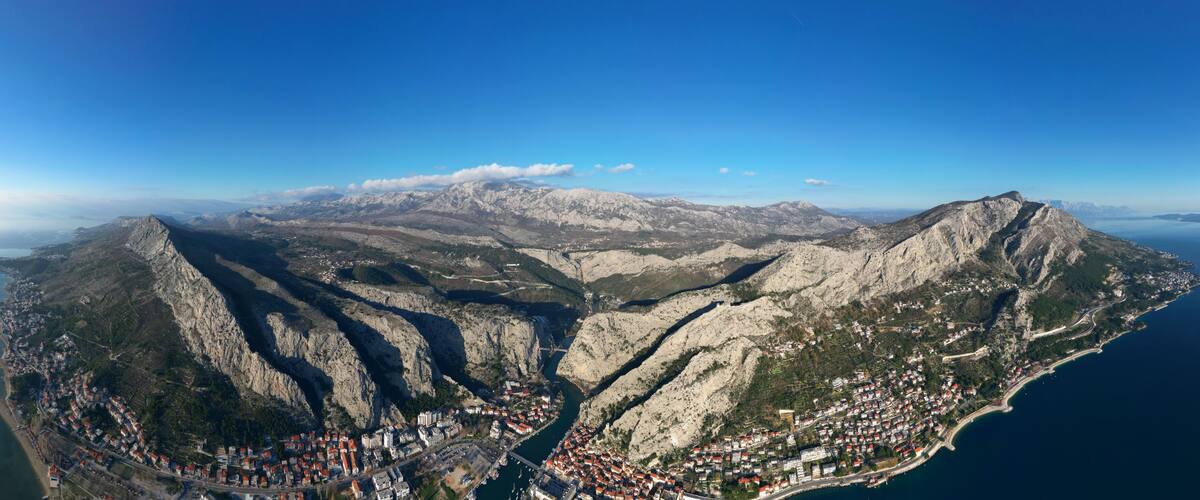 Aerial drone panorama view of Omis town in Croatia. Location is where the Cetina River meets the Adriatic Sea. Beautiful city next to the mountains and the sea. Travel and holidays destination.