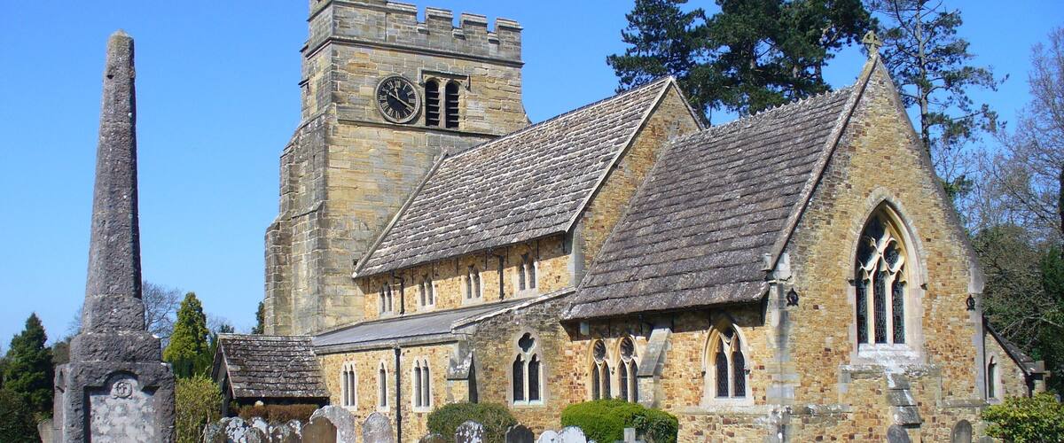 A historic church with a tall clock tower and a prominent stone monument in the foreground.