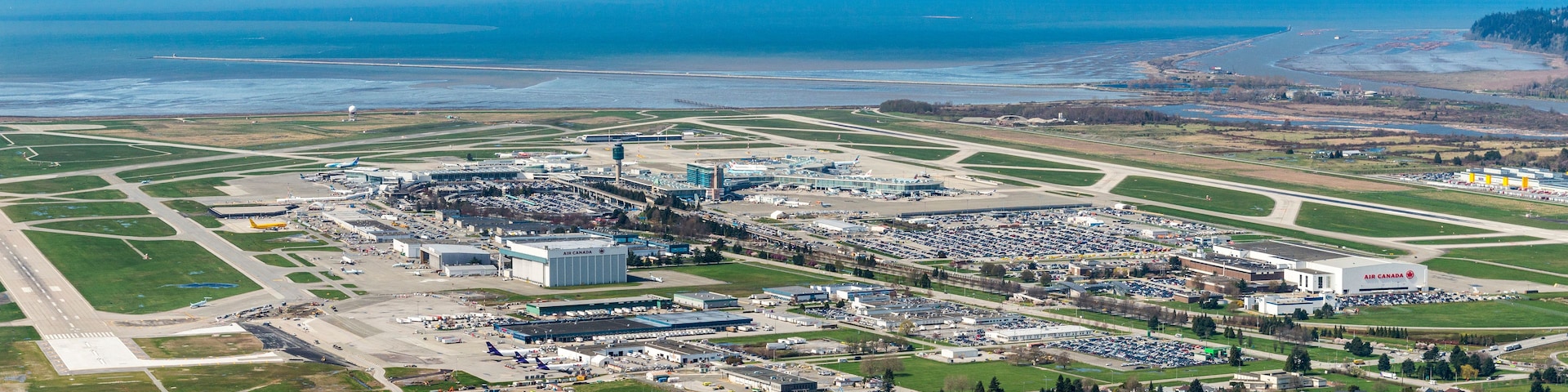 Un aéroport doté de plusieurs pistes, d’un grand bâtiment terminal et d’une étendue d’eau au premier plan.