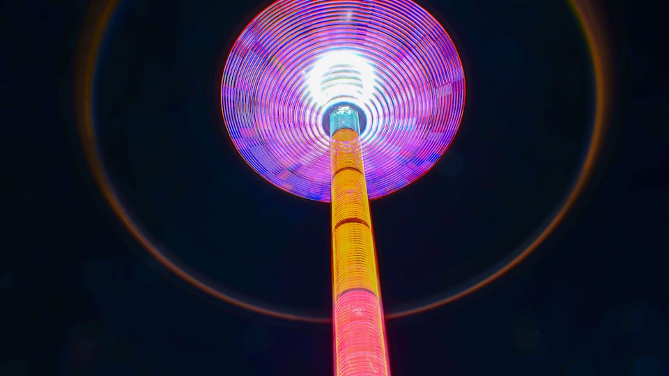 A tall, illuminated structure with a circular top and a vertical pole.