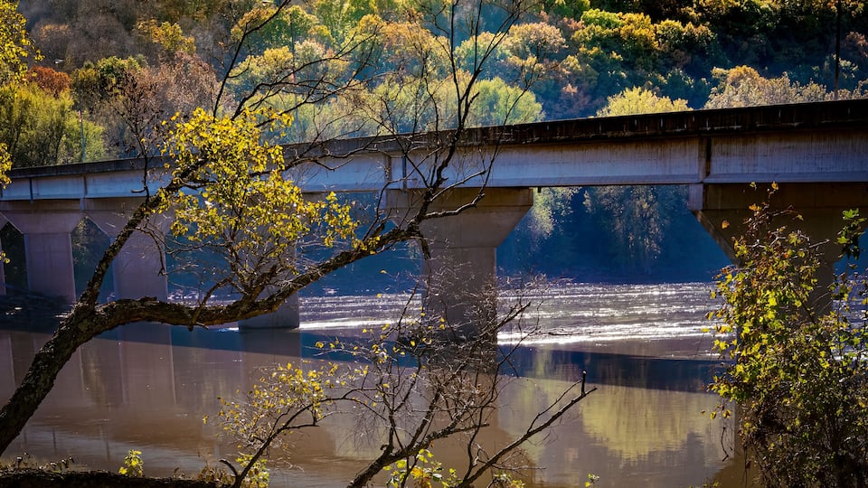 A bridge over a river with surrounding trees and hills.