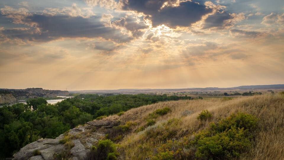 Un paisaje con río, colinas y cielo nublado.