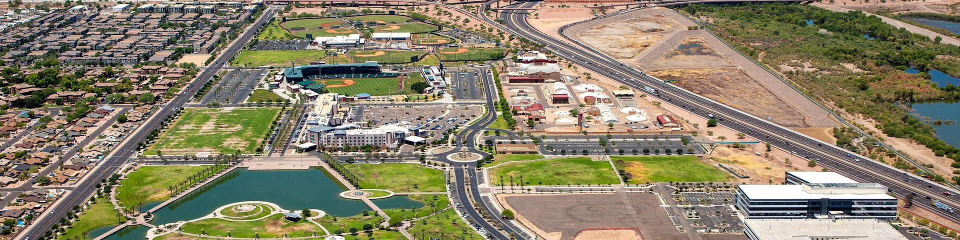 An aerial view of a city with a large stadium, parking lots, and a river.