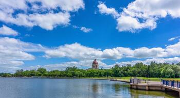 A lake with a bridge, a park with trees, and a large building with a dome in the background.