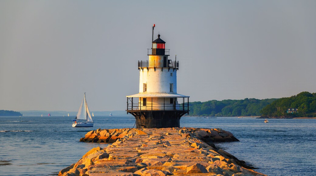 A lighthouse on a rocky pier with sailboats in the background.