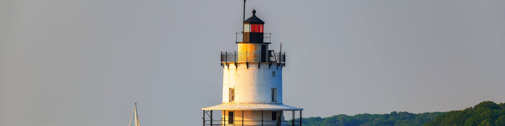 A lighthouse on a rocky pier with sailboats in the background.