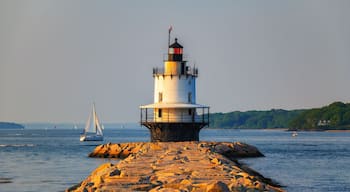 A lighthouse on a rocky pier with sailboats in the background.