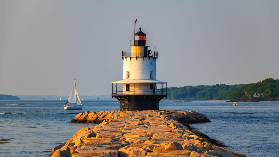 A lighthouse on a rocky pier with sailboats in the background.
