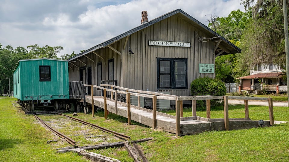 A historic train depot with a wooden structure, a covered waiting area, and a small green caboose.