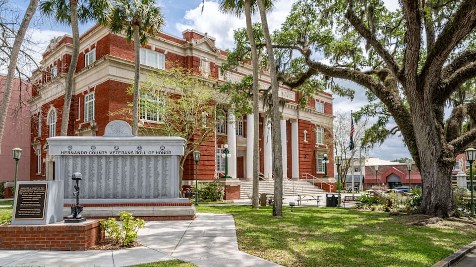 A historic building with a red brick facade, a large tree in the foreground, and a memorial plaque.