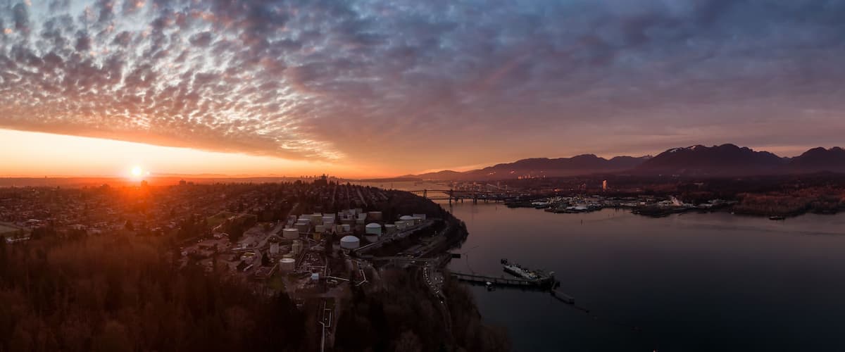 Ein Sonnenuntergang über einer Stadt mit einem Fluss, Bergen im Hintergrund und einer Brücke.